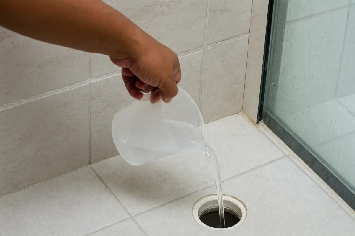 Cheiro Ruim no Ralo do Banheiro: Causas e Como Eliminar 2 Mão despejando água de uma jarra plástica em um ralo de piso de banheiro