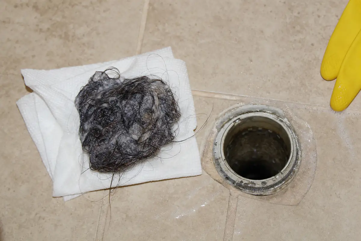 Bolo de cabelo com resíduo de sabão sobre papel toalha ao lado do ralo do chuveiro aberto