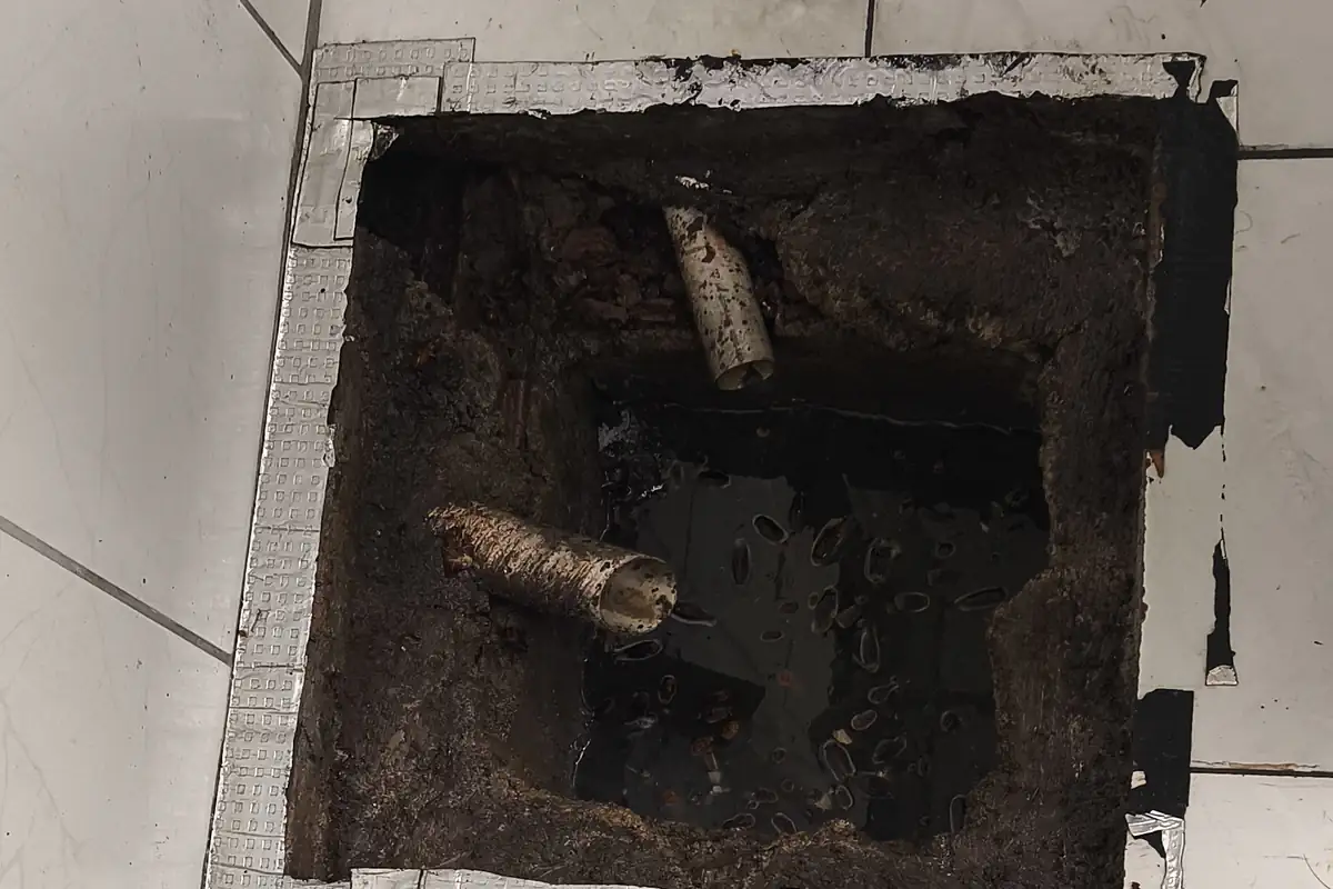 Caixa de Passagem para Esgoto: O Que É, Quando Usar, Medidas 1 Caixa de esgoto no piso de área molhada com a tampa removida, mostrando as tubulações internas