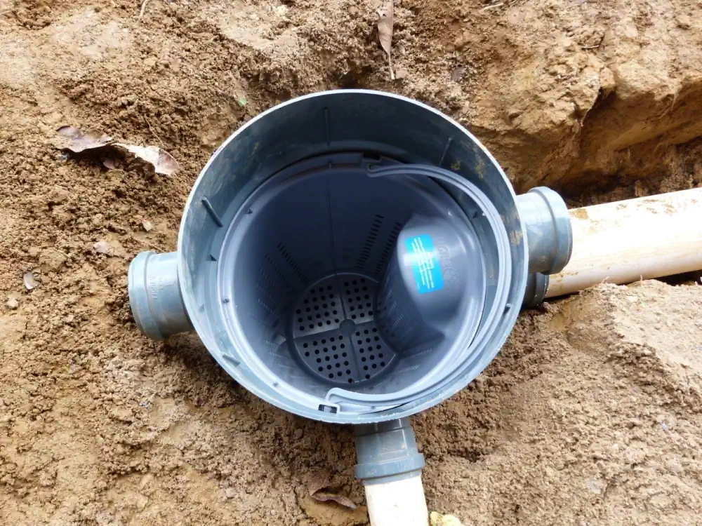 Caixa de gordura de PVC instalada em vala, vista de cima, com o cesto interno e os tubos de entrada e saída