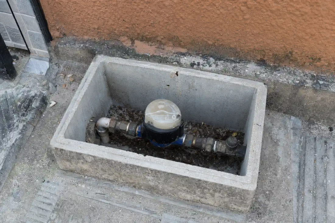 Religação de Água Sanepar: Como Pedir Depois do Corte 1 Caixa de concreto aberta na calçada com o hidrômetro de uma residência à mostra