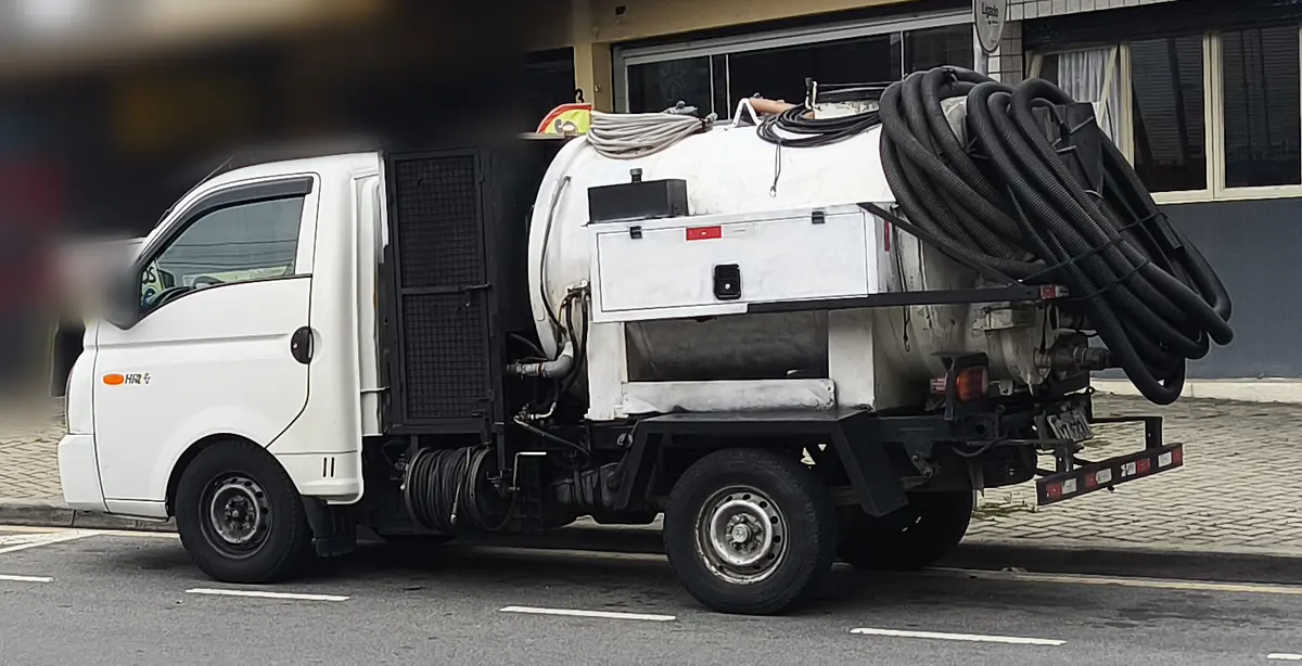 Caminhão de limpeza de fossa e hidrojateamento, com tanque branco e mangueira preta enrolada, estacionado em rua de Curitiba
