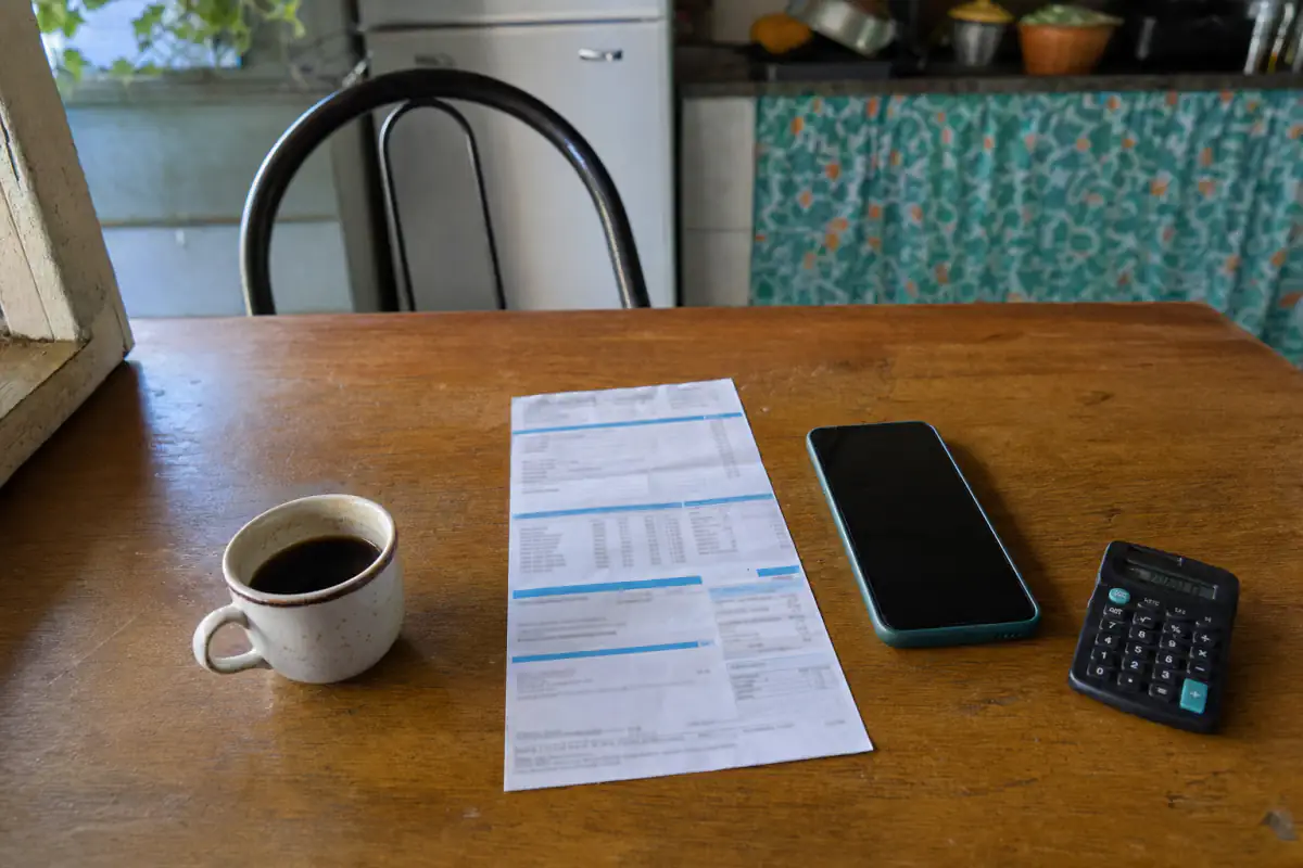 Sanepar fatura: conta de água impressa sobre a mesa da cozinha, com celular, calculadora e uma xícara de café