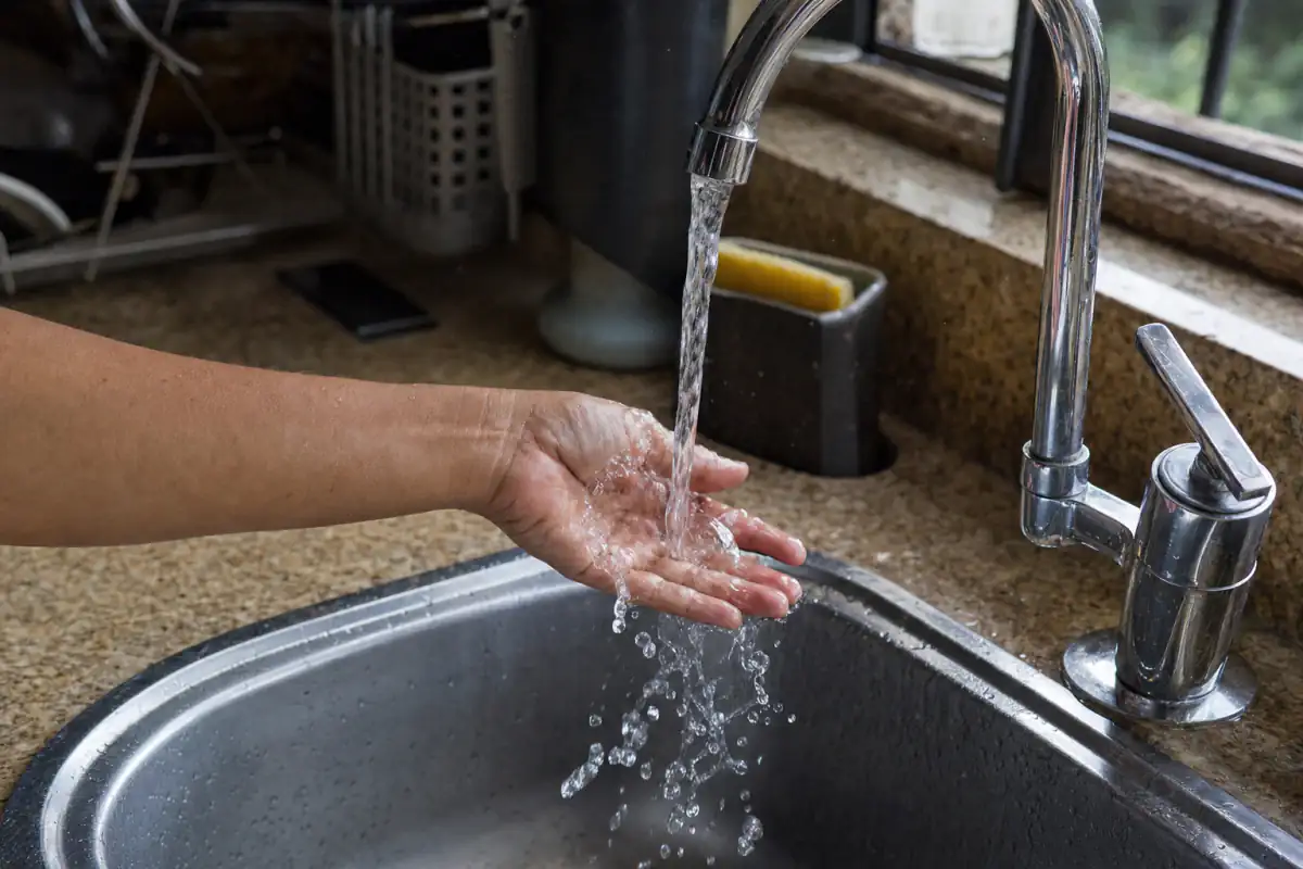 Religação de água Sanepar: mão sob uma torneira de cozinha com a água voltando a correr na pia