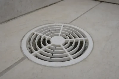 Cheiro ruim no ralo do banheiro: ralo seco de plástico branco com poeira e fios de cabelo na grelha