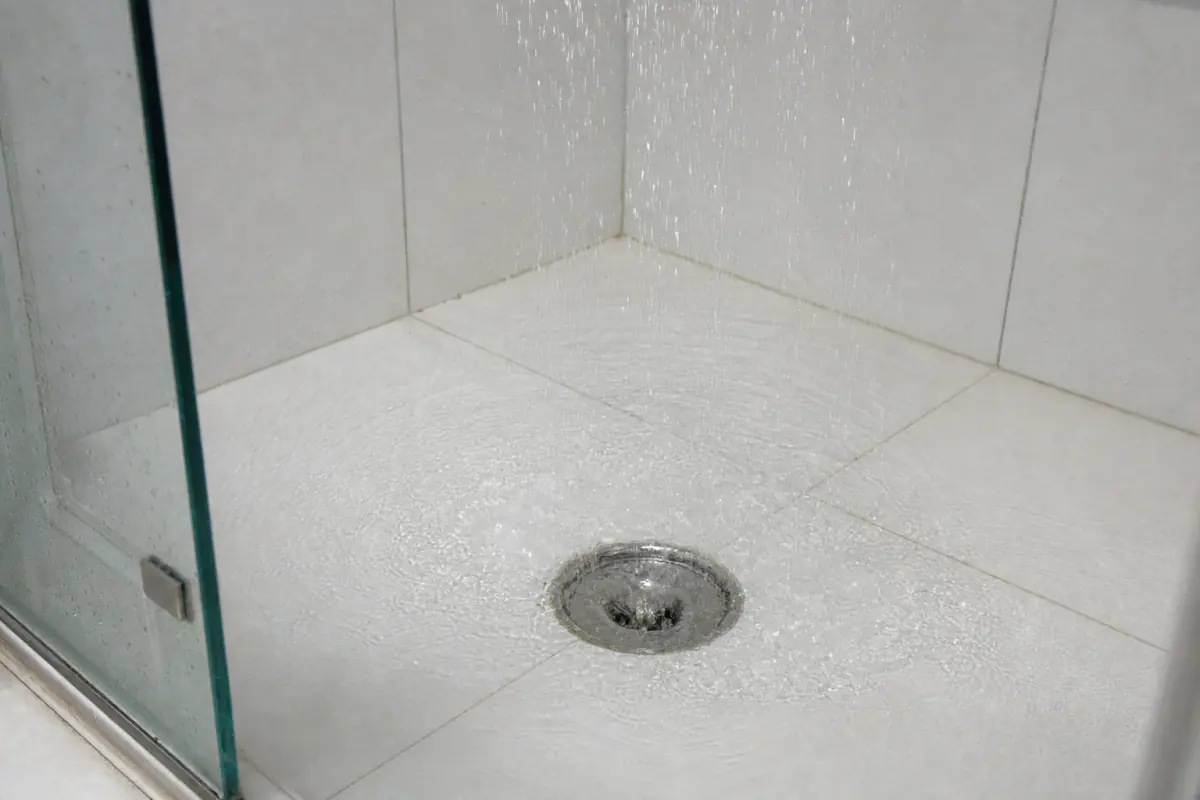 Água do chuveiro escoando livremente pelo ralo de aço inox de um box limpo