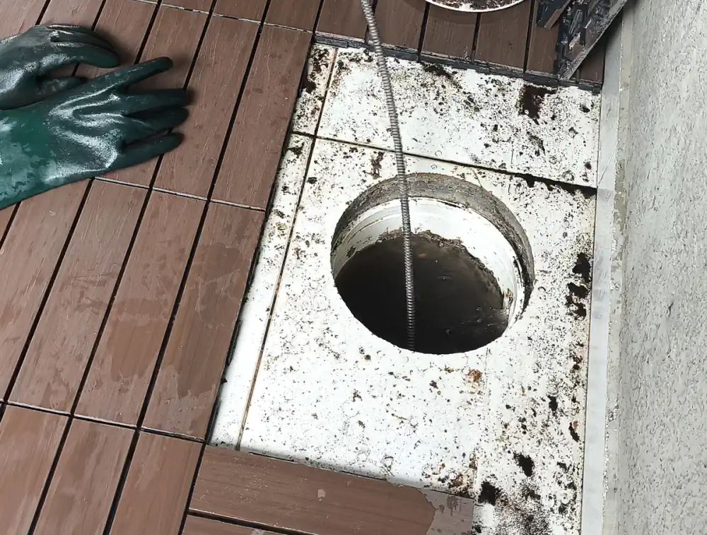 Ralo externo de um deck aberto, sem a grelha, com o cabo de uma máquina de desentupir entrando no ralo