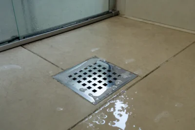 Vazamento ralo banheiro: água e espuma de sabão empoçadas em volta da grelha do ralo sobre piso de cerâmica bege
