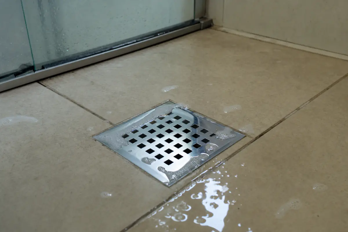 Vazamento ralo banheiro: água e espuma de sabão empoçadas em volta da grelha do ralo sobre piso de cerâmica bege
