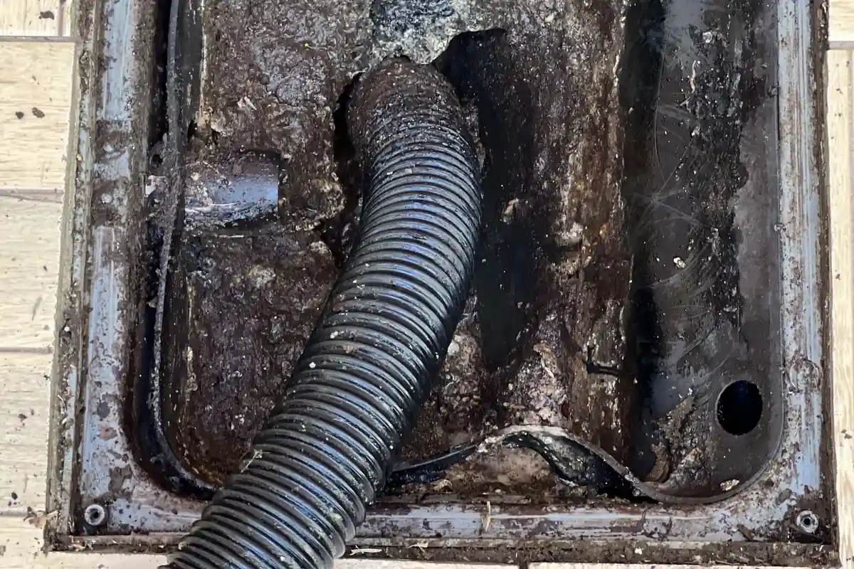 Produto para Limpar Caixa de Gordura: O Que Usar e Evitar 3 Interior de uma caixa de gordura aberta, com gordura escura nas paredes e uma mangueira corrugada preta de sucção apoiada no fundo