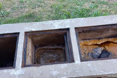 Caixa de gordura de concreto com três compartimentos alinhados no gramado, com gordura alaranjada endurecida no compartimento da direita