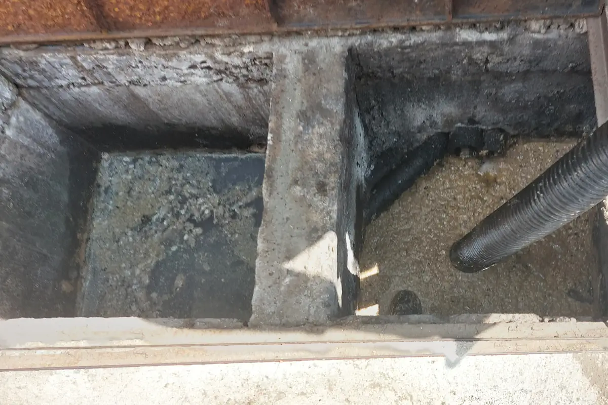 Caixa de Gordura: O Que É, Como Funciona e Como Limpar 1 Caixa de gordura de alvenaria com duas câmaras divididas por uma parede e mangueira de sucção preta entrando na câmara da direita