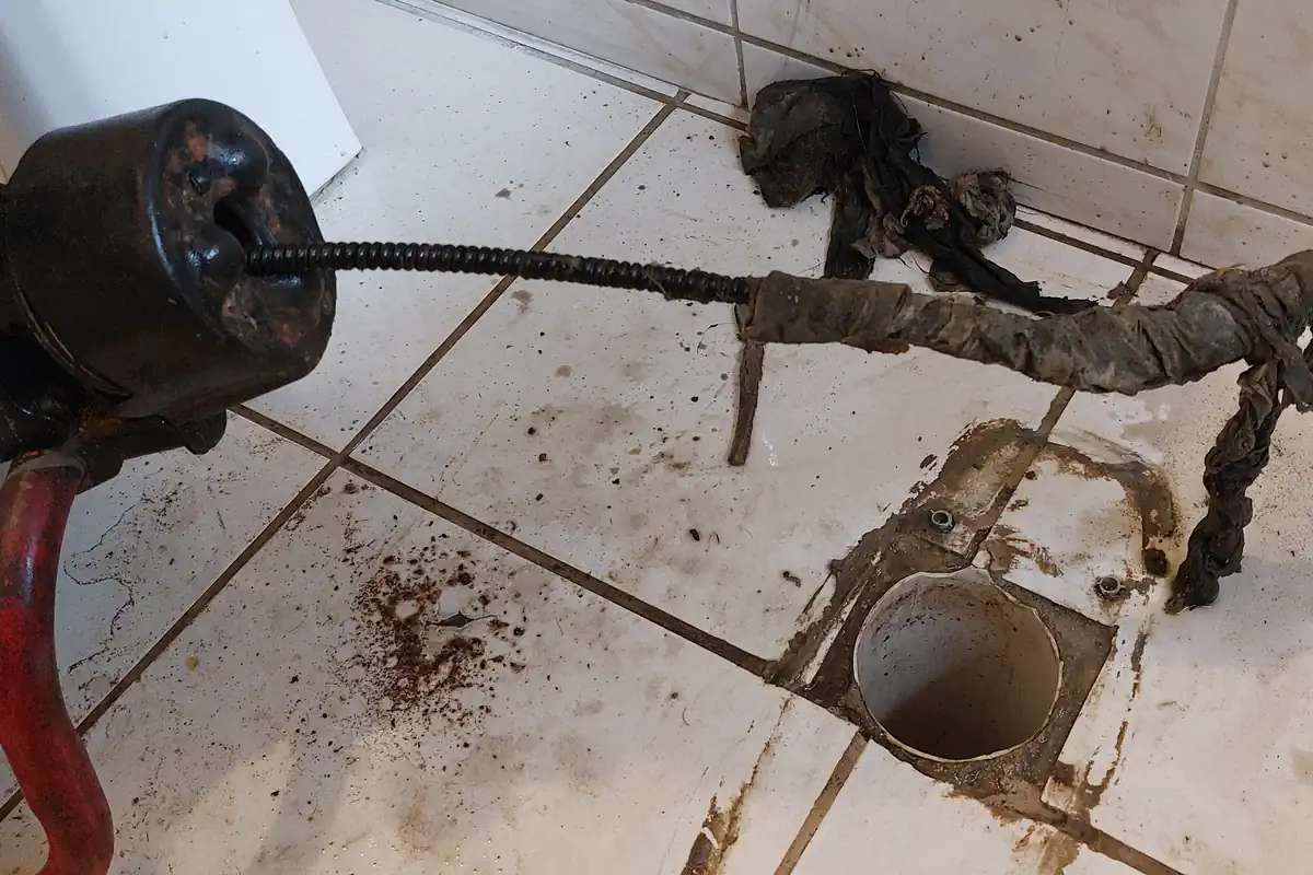 Como Desentupir Pia de Cozinha: Passo a Passo Seguro 2 Cabo flexível de uma máquina de desentupimento ao lado de panos e resíduos retirados de um ralo de piso aberto