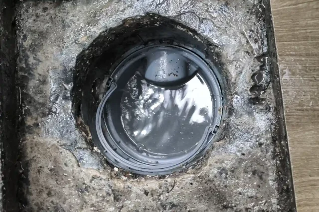 Ralo de piso aberto visto de cima, com a tampa de vedação no meio e gordura acumulada ao redor da borda